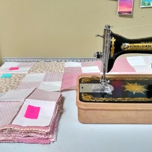 A sewing machine and stacks of patchwork quilt squares with post-it notes on top of each stack