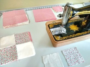 A quilter's workspace including a vintage Singer sewing machine and squares of quilting cotton in the process of being pieced together