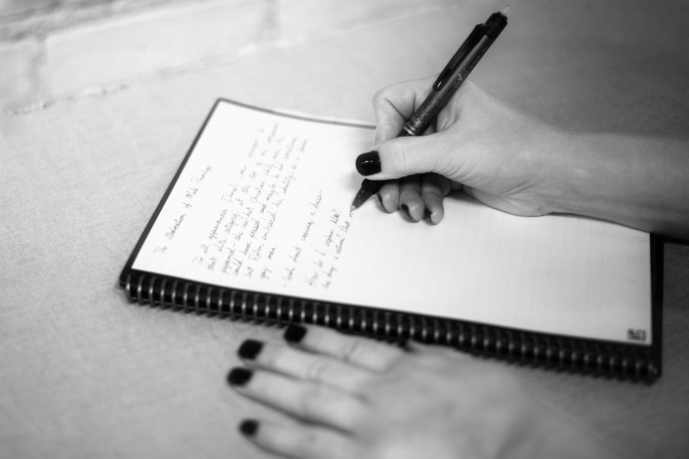 A black and white photo of hands writing in a notebook