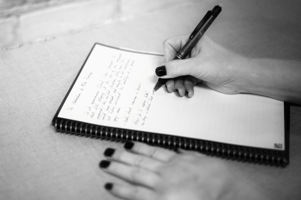 A black and white photo of hands writing in a notebook