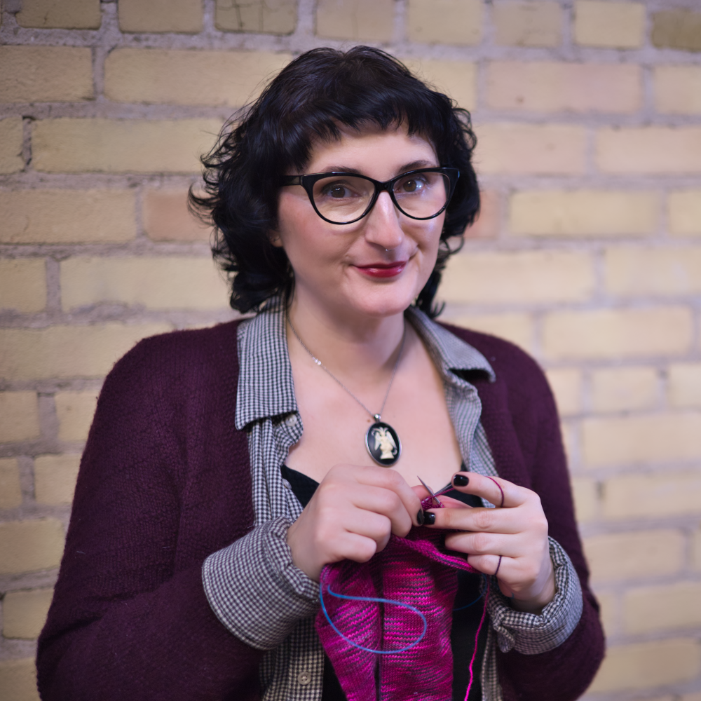 The author smiling at the camera and knitting